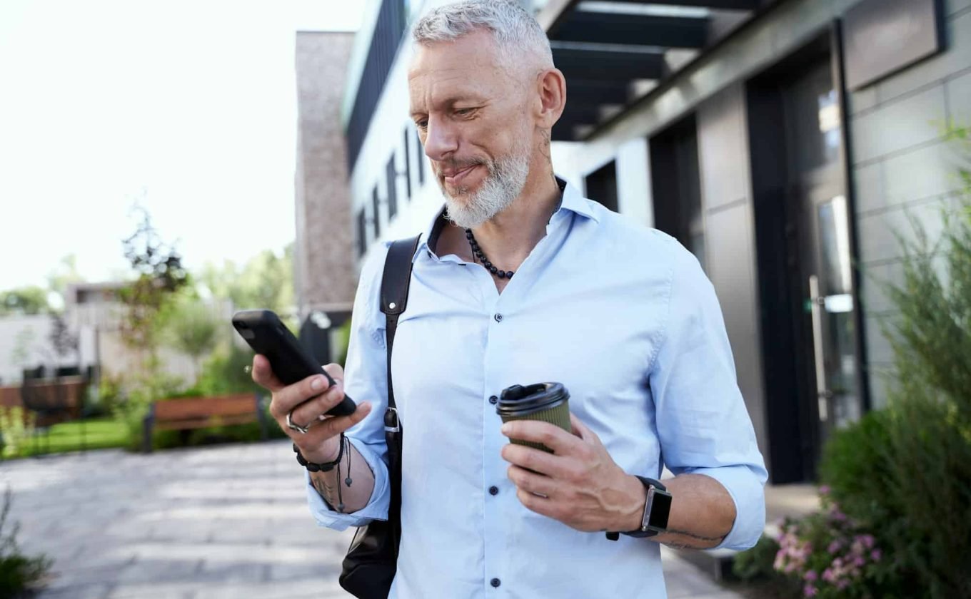 Stay connected. Modern middle aged businessman using his smartphone while walking outdoors with a