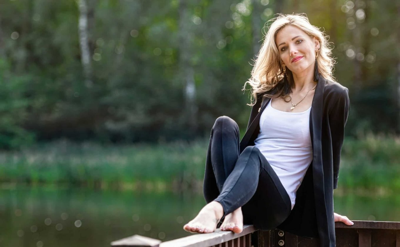 young positive, smiling female sits on the wooden railings of the pier